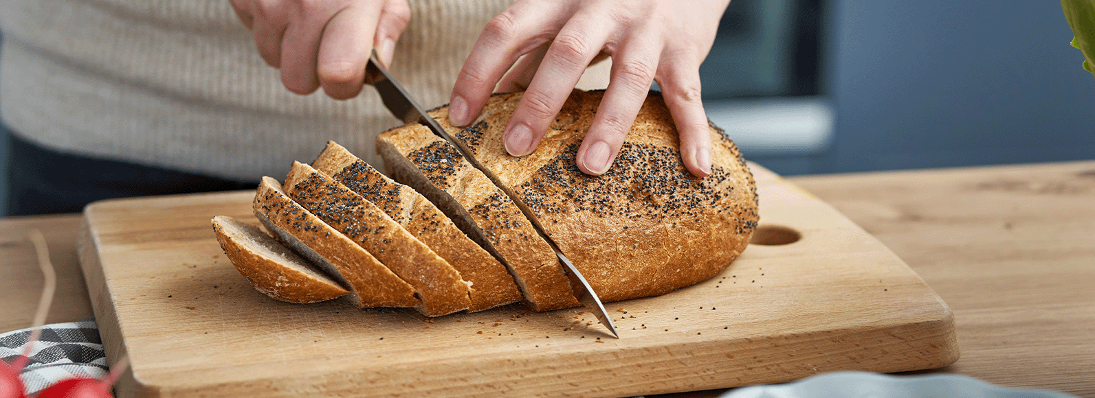 Foto de um pão sendo cortado em um ambiente que se não for controlado pode favorecer a contaminação cruzada.